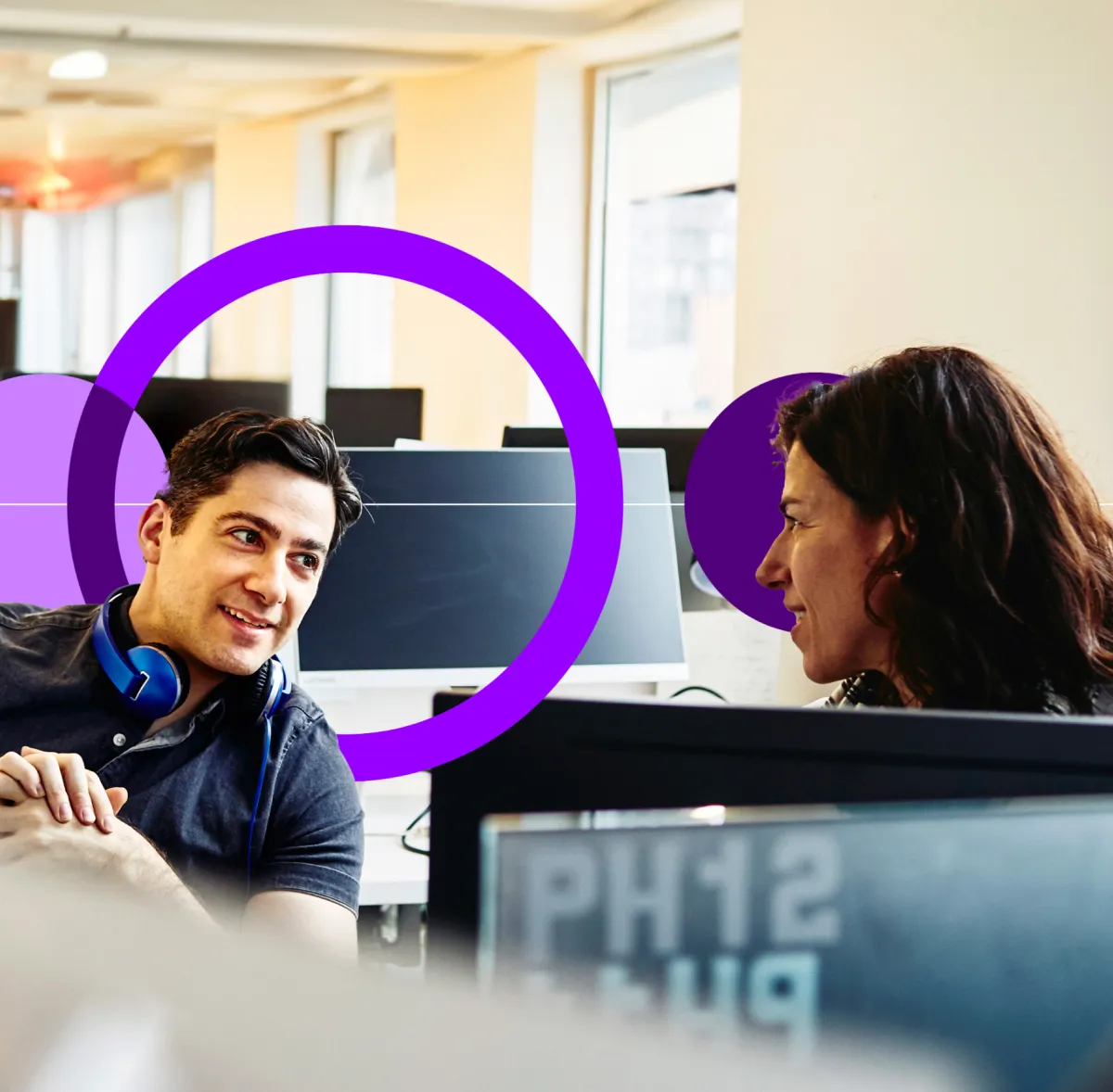 Un homme et une femme en pleine conversation, assis à un bureau dans un bureau avec des ordinateurs.